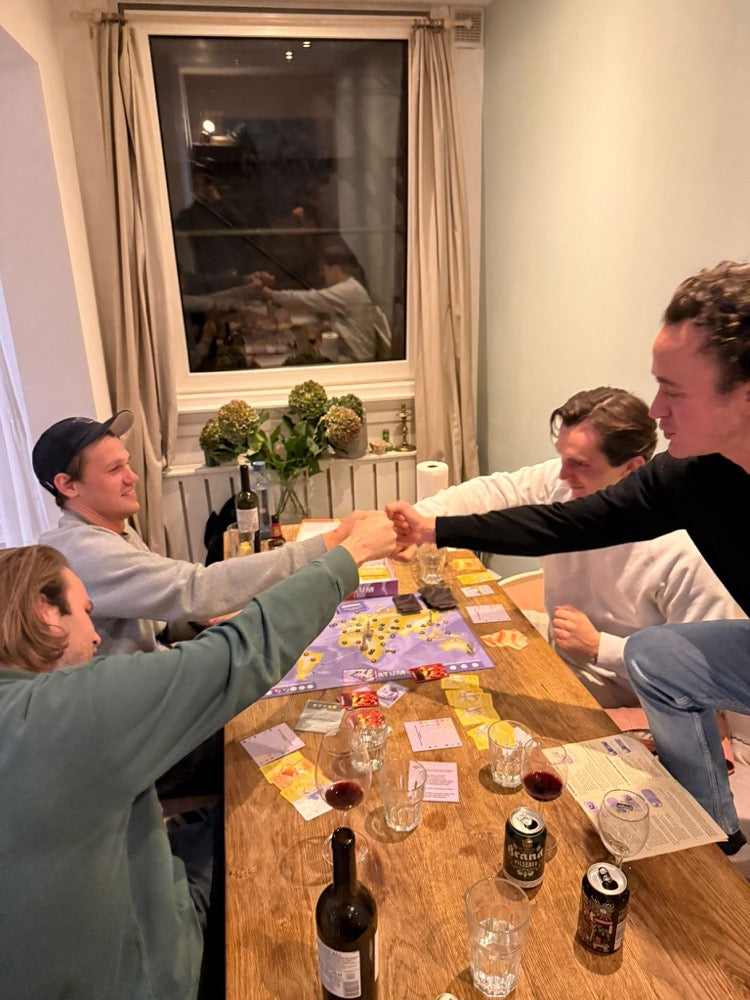 Vrienden aan een houten tafel met wijn schudden elkaar de hand boven het bord van Ultimatum